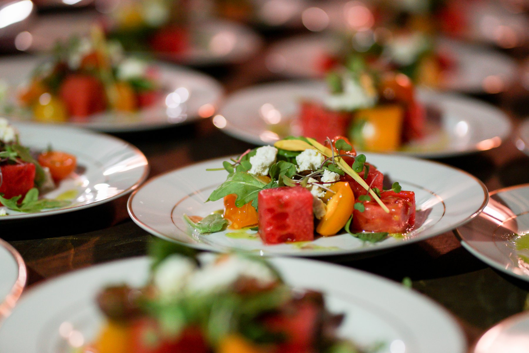 Rows of plated heirloom tomato and watermelon salads with arugula and goat cheese at a Hamptons benefit dinner