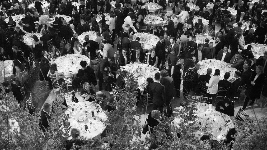 Overhead view of a black-tie gala dinner in New York City, with round banquet tables, candlelight, and tall greenery centerpieces